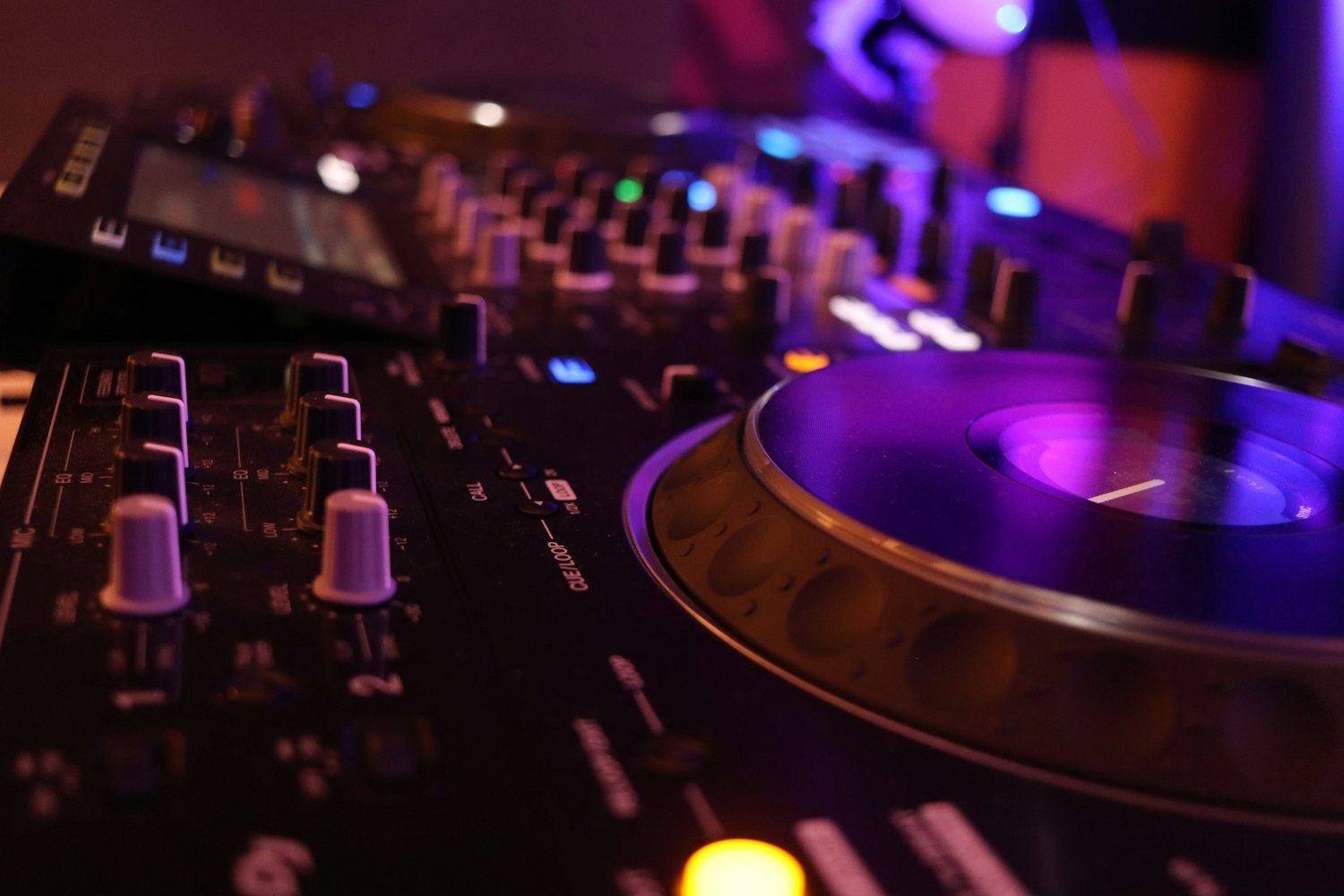 A DJ mixer and turntable platter lit in club purple