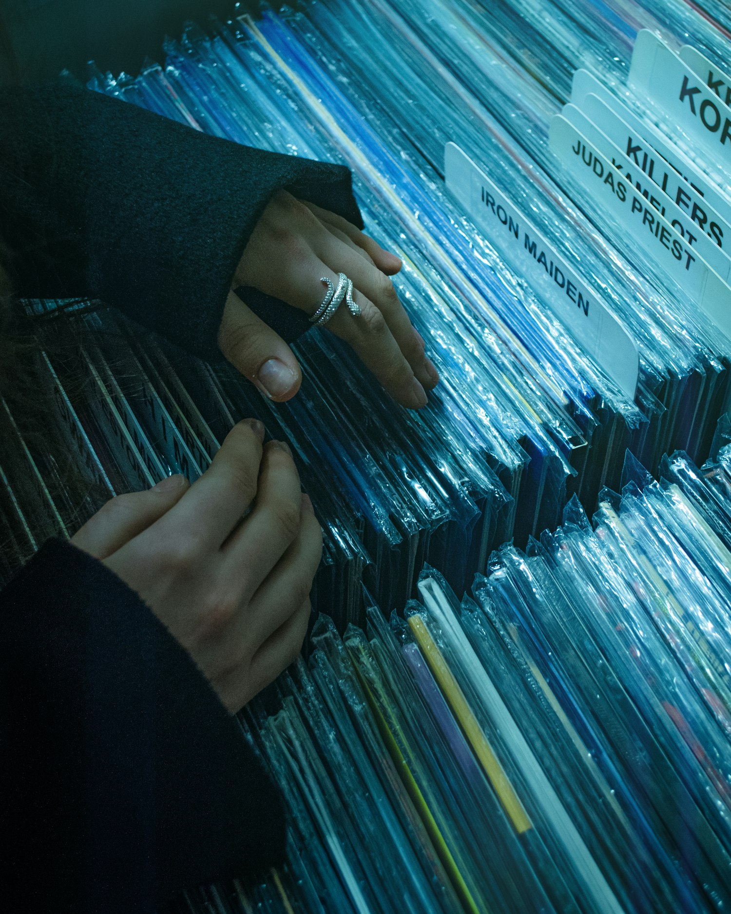 Hands flipping through records in a crate, lit cold and blue
