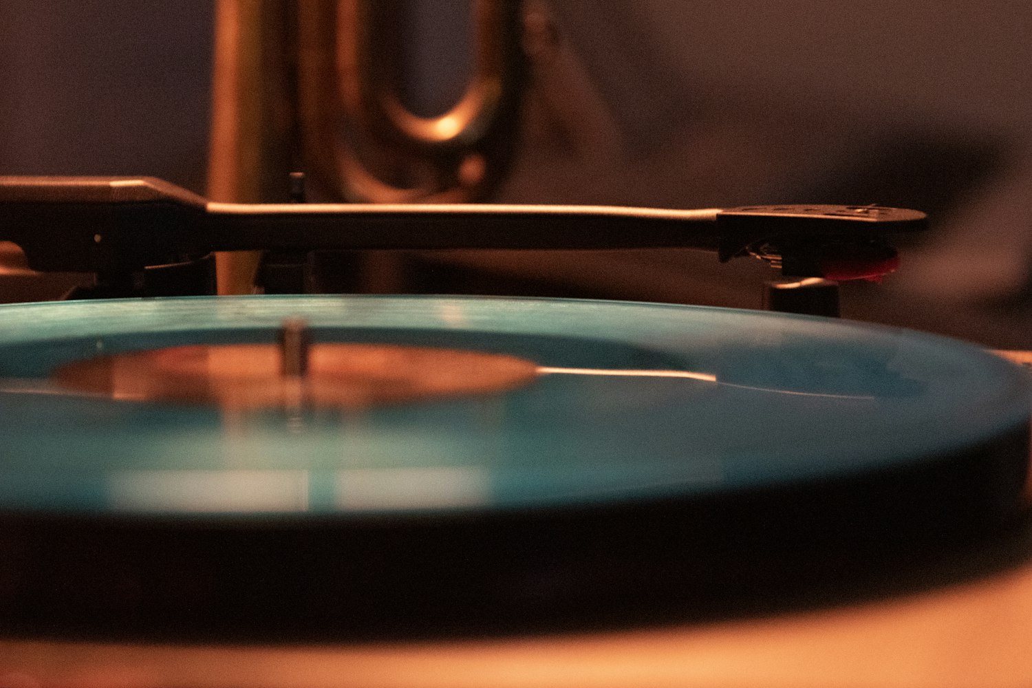 A record spinning on a turntable under warm amber light beside a brass horn